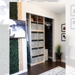 A modern closet makeover with IKEA Kallax shelves, decorated with monochrome patterned storage bins. The closet is flanked by green foliage panels and minimalist art. There's a textured rug on the dark wooden floor.