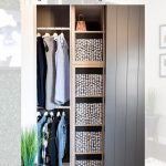 A neatly organized closet featuring IKEA Kallax shelves with black and white storage bins, hanging clothes on the left, and decor such as a plant and TV artwork. The space is modern and inviting.