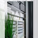 A neatly organized linen closet featuring IKEA TROFAST storage units, folded white towels, patterned bins on the top shelf, and a decorative plant. The door is partially open, and the interior is bright and tidy.