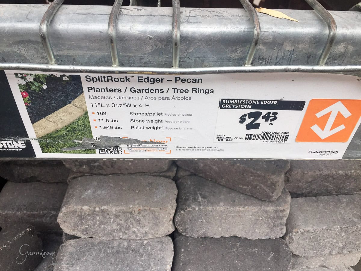 A label for SplitRock Edger - Pecan is attached to a metal rack, displaying specifications: 168 stones per pallet, 11.4 lbs each. Price is $243, identified as RumbleStone Edger Greystone. Some stacked stones are visible below.