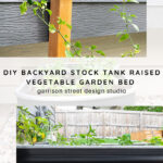A black metal stock tank serves as a raised garden bed filled with green vegetable plants, set against a wooden fence. A humorous "Stayin' Alive" chalkboard plant marker is in the soil.