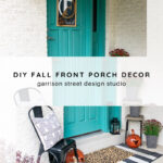 A teal front door is decorated for fall with pumpkins, a black chair with a pillow, potted plants, a black-and-white rug, and a framed initial door hanger. The scene is titled "DIY Fall Front Porch Decor.