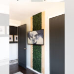 A modern room with dark doors, white walls, and a TV mounted above a faux green living wall with vertical wood accents. Text above reads: "DIY Faux Green Living Wall Behind a TV, garrison street design studio.
