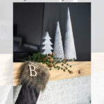 A mantel decorated with faux pottery Christmas trees, a fur-trimmed stocking with a "B" initial, pine garland, and a white brick wall, styled by Garrison Street Design Studio.