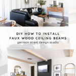 A modern living room with faux wood ceiling beams, a black sectional sofa, tan rug, and wooden console table with decor. The space features white paneled walls, a fireplace, and neutral accent pieces. Instructions for ceiling beams included.