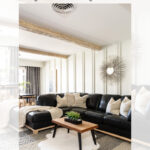 A modern living room with a black sectional sofa, neutral throw pillows, a wooden coffee table, and faux wood ceiling beams. Sunburst wall art and large windows add brightness to the space. Text above reads, "DIY how to install faux wood ceiling beams.