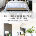 A modern boho bedroom with a dark accent wall, brass and white decor, a bed with a white comforter, patterned pillows, two-toned nightstands, and a dresser with a round mirror and greenery. Text reads: DIY Modern Boho Bedroom Makeover Reveal.