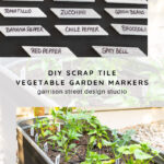 Labeled white tile markers identifying various vegetables and herbs are shown, both up close and placed in a raised garden bed with young plants. Text reads: “DIY Scrap Tile Vegetable Garden Markers.”.
