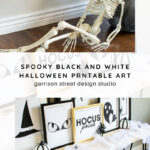 A plastic skeleton leans against a wall with spiderweb decor above. Below, a shelf displays black-and-white framed Halloween art, mini pumpkins, and more spiderwebs, creating a spooky scene.
