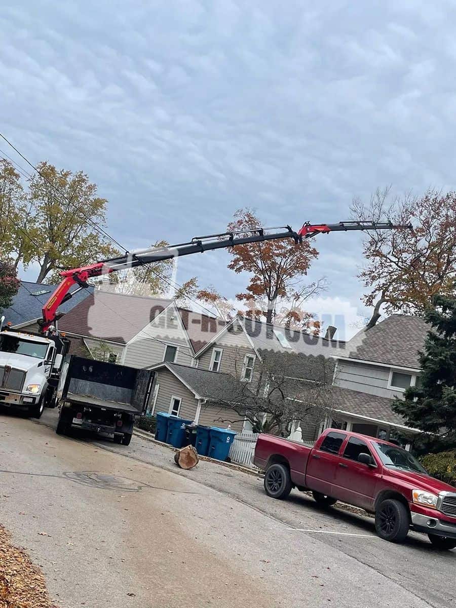 Tree trimming bucket truck with extended arm over houses and street.