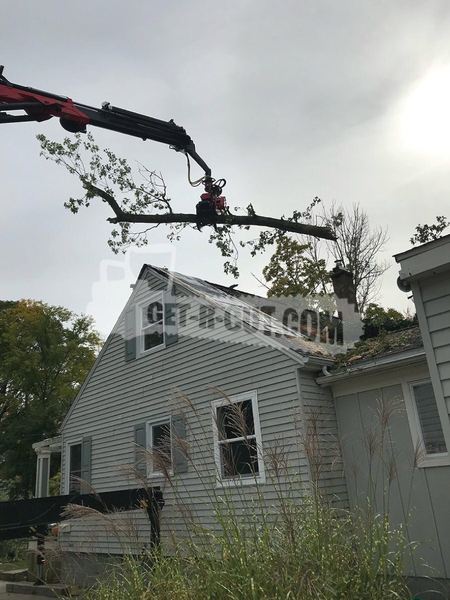 Tree trimming or removal using crane equipment on residential property.