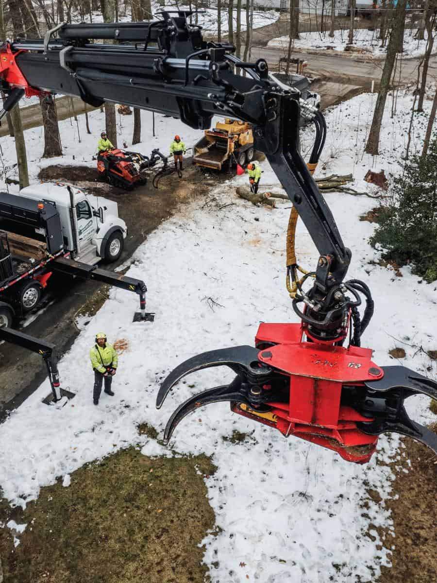 Large hydraulic tree cutting machine with workers in snowy forest.