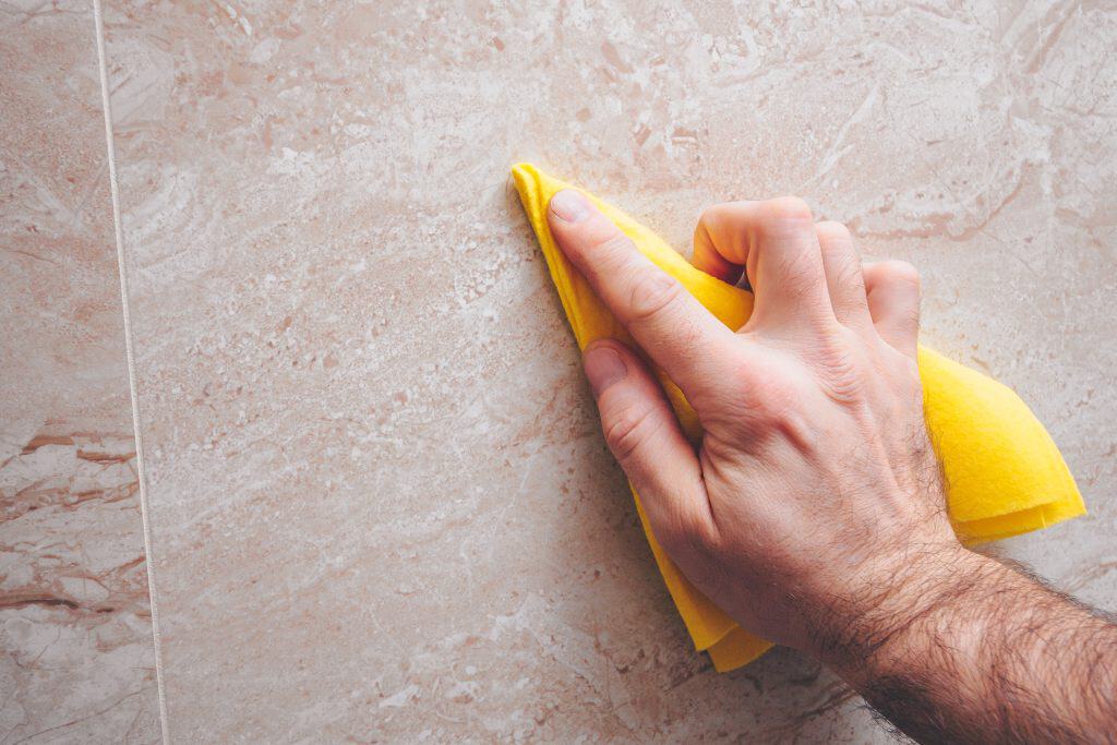 Hand cleaning beige granite countertop with yellow cloth.