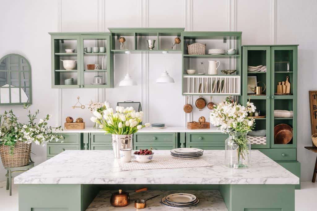 Green kitchen with marble countertop and open shelving for materials overview.