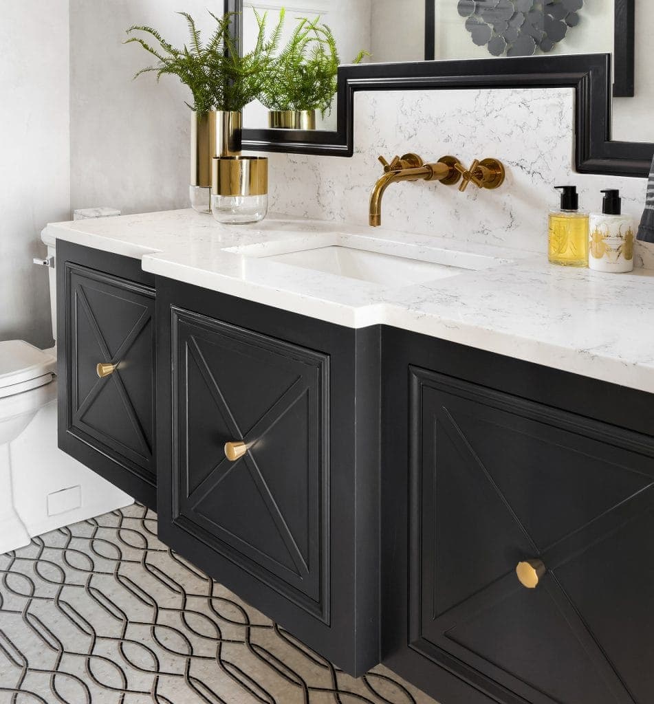 Black bathroom vanity with marble countertop, gold faucet, and decorative accessories.
