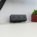 Power strip with three outlets and a small green plant on a white desk.