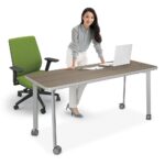 Woman standing at a modern office desk with a green chair and laptop.