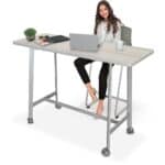 Woman sitting at a height-adjustable desk with laptop and office supplies.