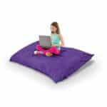 Young girl sitting on a purple bean bag with a laptop.
