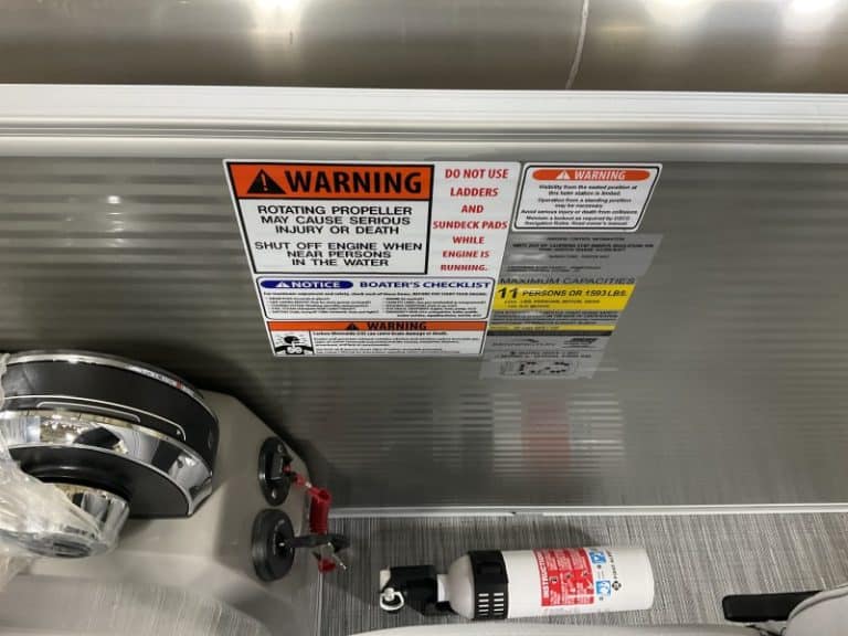 Warning labels on boat storage tank with safety instructions and capacity info.
