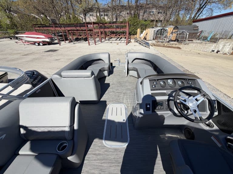 Boat dashboard with steering wheel, gauges, and seating in an outdoor storage yard.
