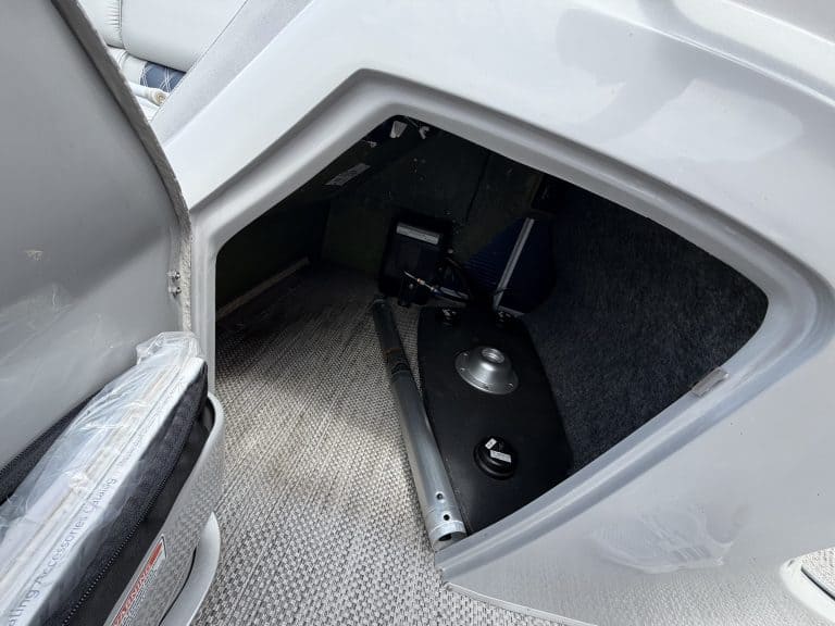 Open storage compartment of a Bennington 25QSB boat showing equipment inside.