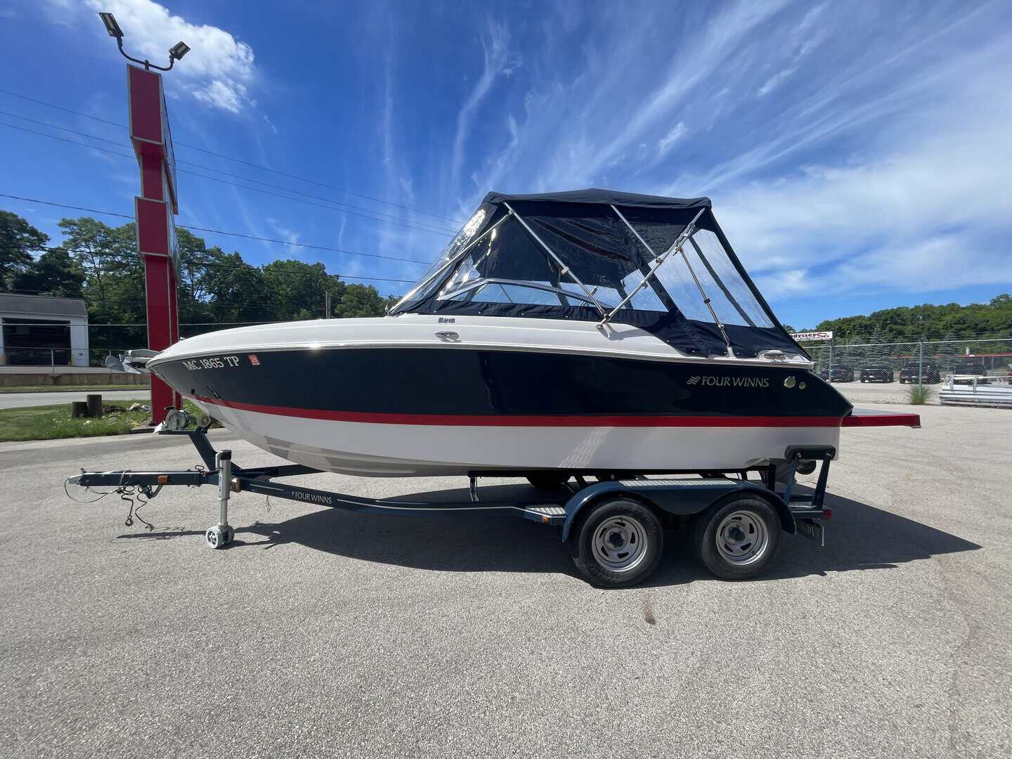 Black and white Four Winns 215 SUNDOWNER boat on trailer at marina.