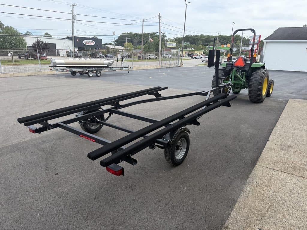 Green tractor with boat trailer attachment on paved lot.