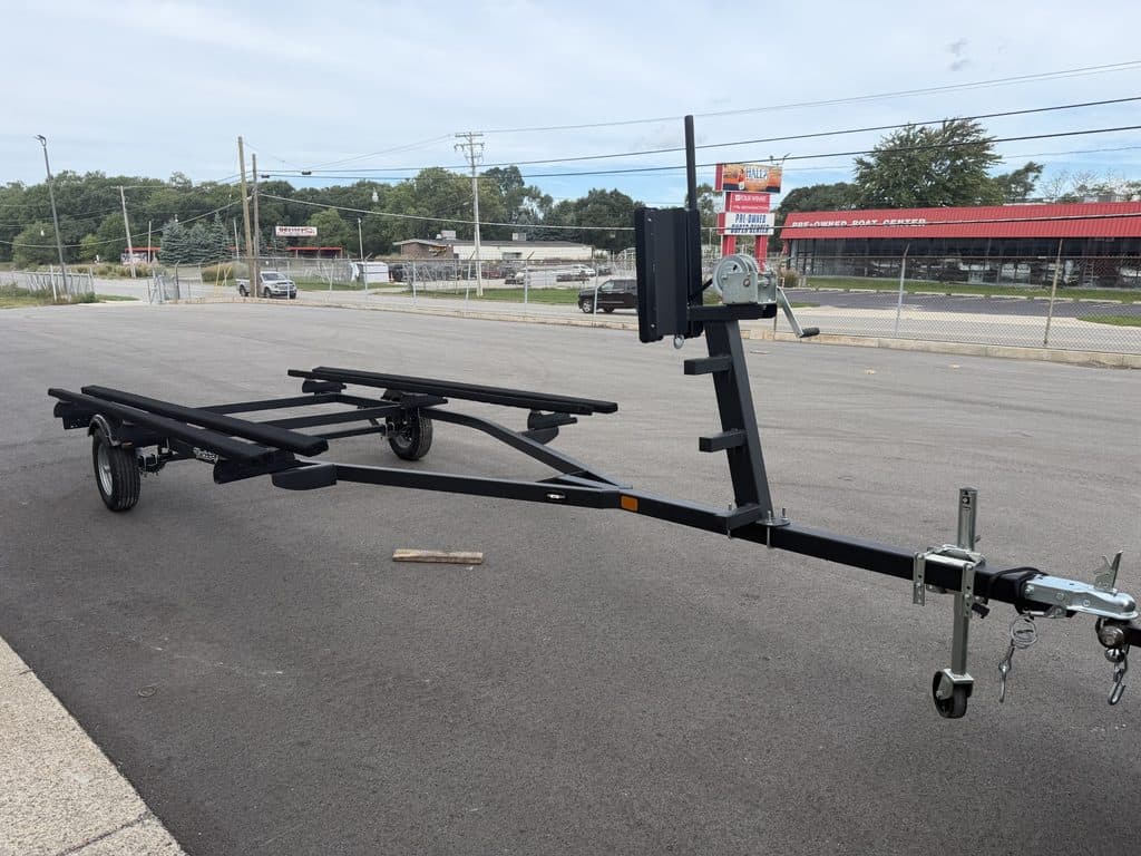 Boat trailer parked on asphalt with road and commercial buildings in background.