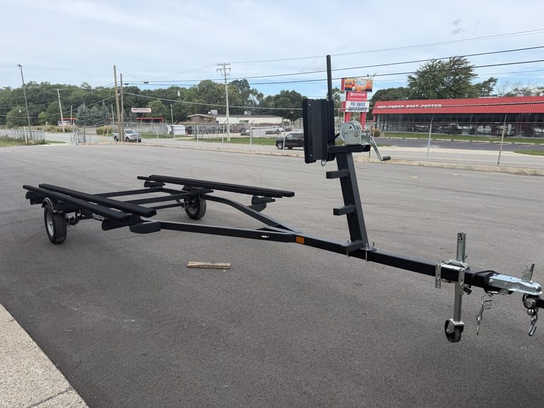 Boat trailer parked on asphalt with road and commercial buildings in background.