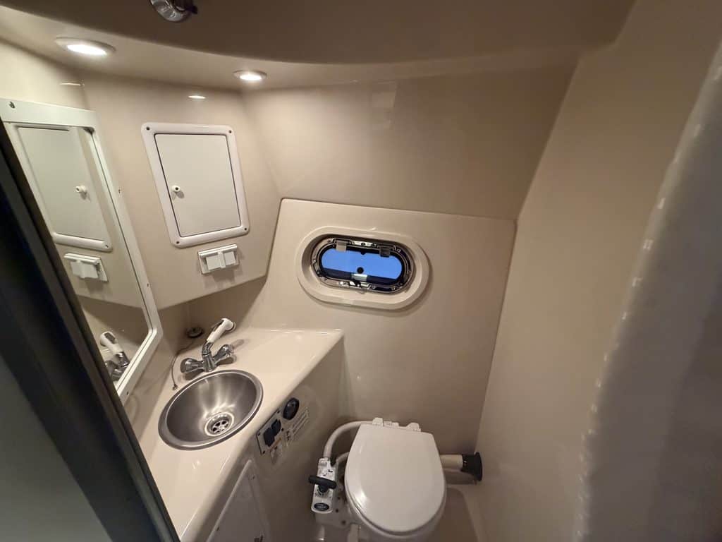 Small boat bathroom with sink, mirror, and porthole window.