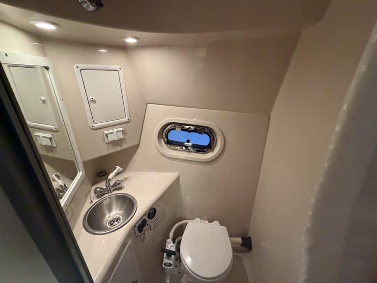 Small boat bathroom with sink, mirror, and porthole window.