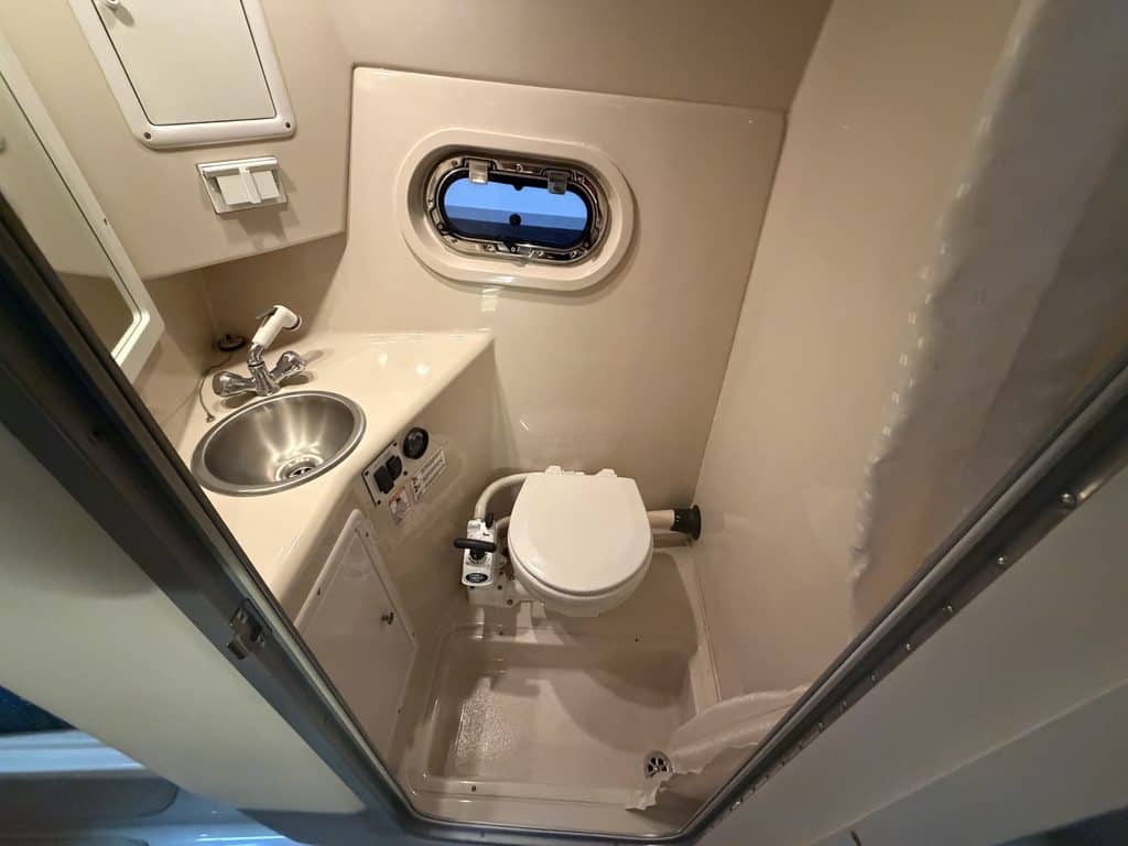 Small boat bathroom with sink, toilet, and porthole window.
