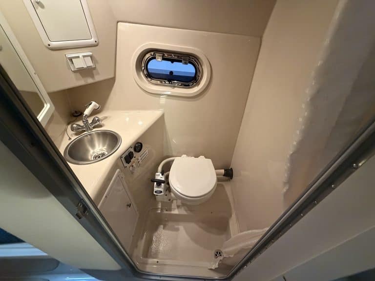 Small boat bathroom with sink, toilet, and porthole window.