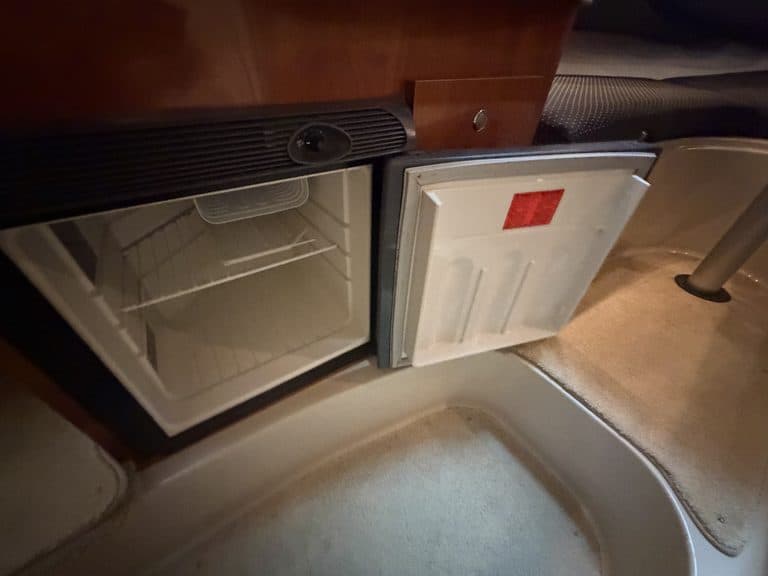 Small built-in refrigerator in boat kitchen with open door showing empty interior.
