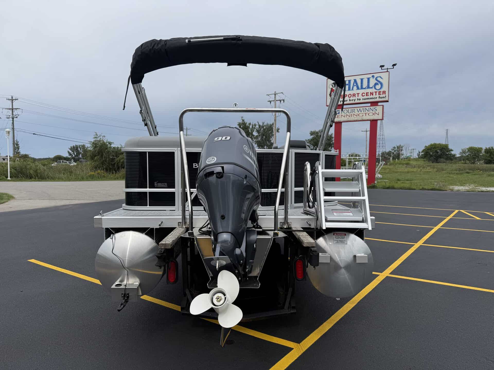 Pontoon boat with outboard motor in parking lot at Hall's Sport Center.