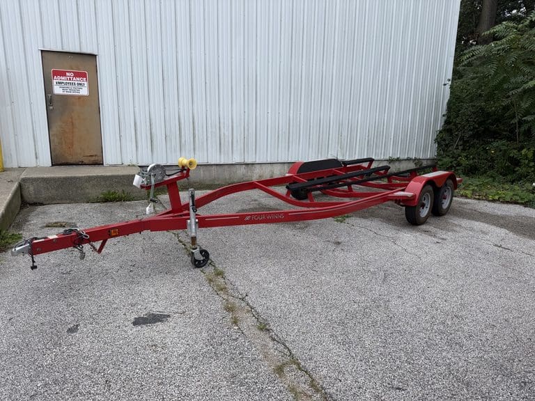 Red boat trailer parked outside a metal building with a no trespassing sign.