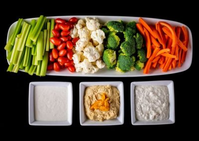 Colorful vegetable platter with celery, cherry tomatoes, cauliflower, broccoli, and carrots with dip.