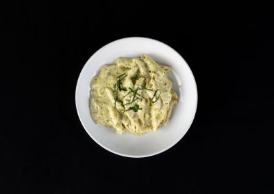 Creamy herb pasta served in a white bowl on a black background.