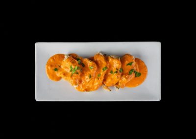 Delicious chicken dish with orange sauce garnished with herbs on a white rectangular plate.
