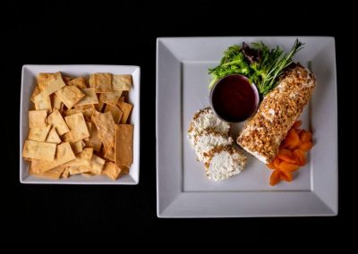 Gourmet dish with spring roll, salad, and dipping sauce on white plate.
