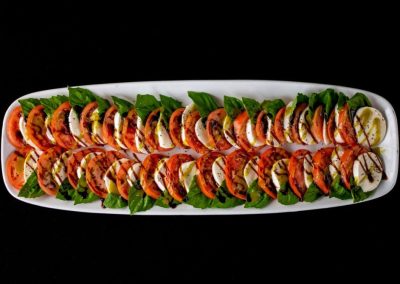 Assorted salmon sushi rolls with lemon slices and greens on a white platter.
