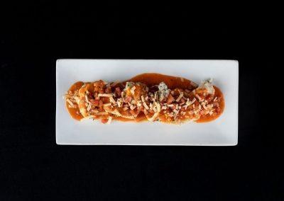 Gourmet spaghetti with sauce, cheese, and toppings on a white rectangular plate.
