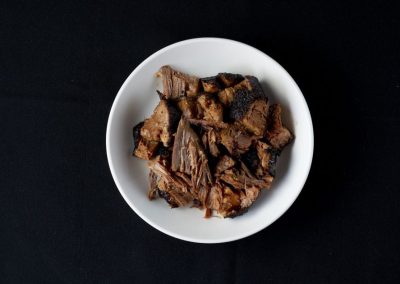 Cooked beef ribs served on a white plate against a black background.