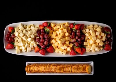 Cheese and fruit platter with strawberries, grapes, and crackers on a black background.