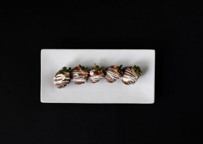 Chocolate-covered strawberries on a white rectangular plate against a black background.