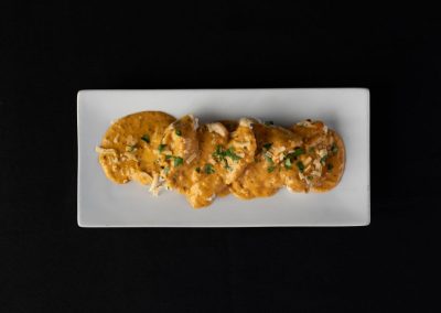 Chicken enchiladas garnished with cheese and herbs on a white rectangular plate.