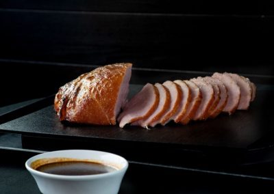 Sliced roast pork served with dipping sauce on black background.