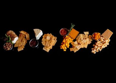 Assorted cheeses, crackers, and snacks on a black background.