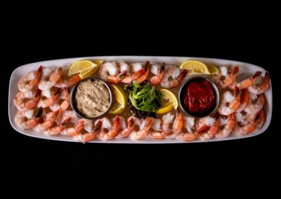 Seafood platter with shrimp, lemon wedges, and dipping sauces on a white plate.